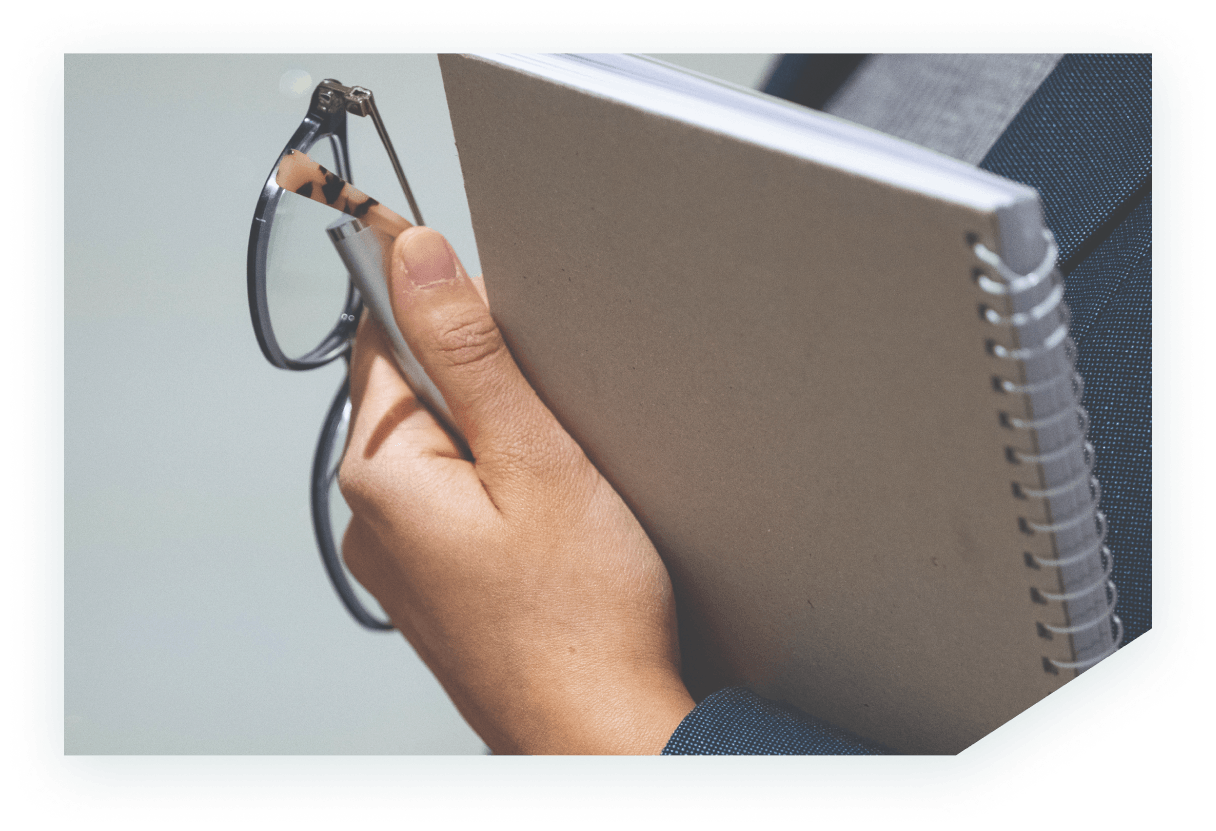 Close up image showing a hand holding a pair of glasses and notebook